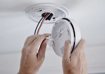 electrician installing wired in smoke detector system